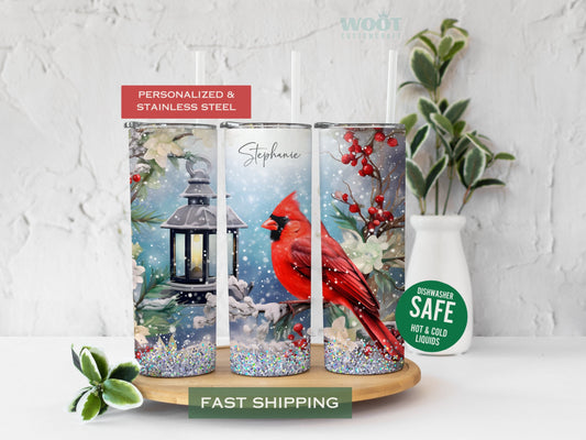 Three tumblers show all sides of a Cardinal bird Tumbler in a tree. It is snowing. There is a snowman there is a lamp flowers, there is glitter, and a personalized name on the top of the tumbler.