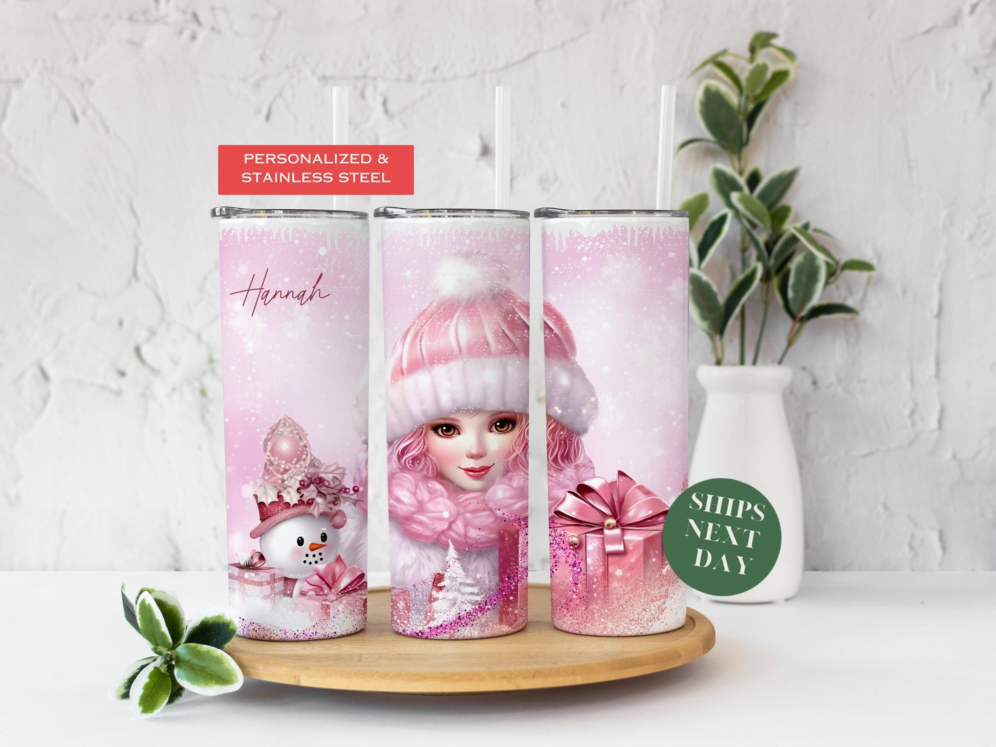 Three tumblers are showing all sides of a Christmas pink Tumbler. It is snowing. There is a girl with pink clothes, a pink hat, pink Christmas packages, a snowman, pink glitter, and a personalized name.
