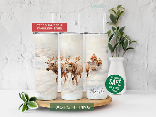 Three tumblers are showing all sides of a Christmas winter Tumbler. It is snowing, and two reindeer are pulling a sleigh with Santa Claus and the personalized name on the button of the tumbler where there is snow.