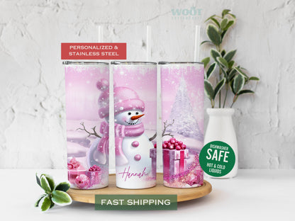 Three tumblers are showing all sides of a Christmas pink Tumbler. It is snowing. There is a snowman with pink clothes and a pink hat, there are pink Christmas packages, there is pink glitter and a personalized name on the button of the tumbler.