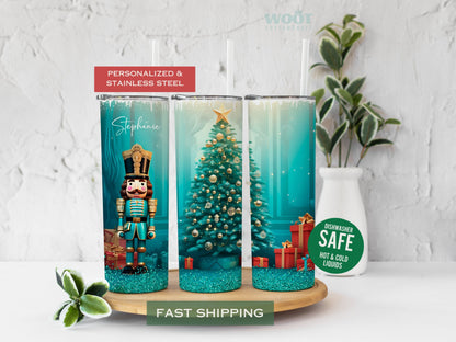 Three tumblers are showing all sides of a Christmas Holiday Tumbler. There is a Nutcracker and a Christmas tree, with Christmas packages and presents on the floor, turquoise glitter, and a personalized name on the top of the tumbler.